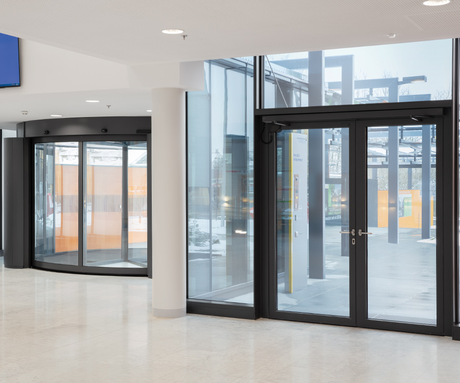 Moderne ingang met draaideuren en glazen wanden, lichte vloer en wit plafond.