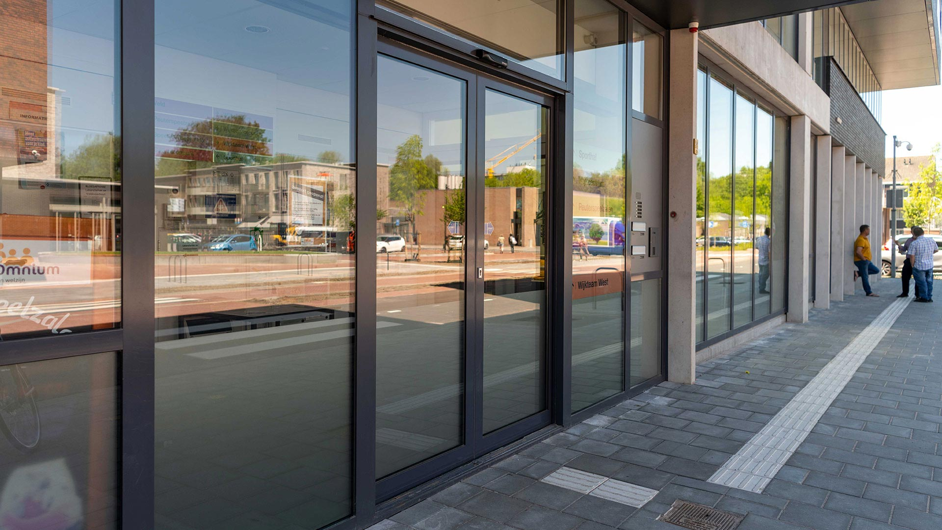 Moderne entree met glazen deuren en mensen op straat in de reflectie.