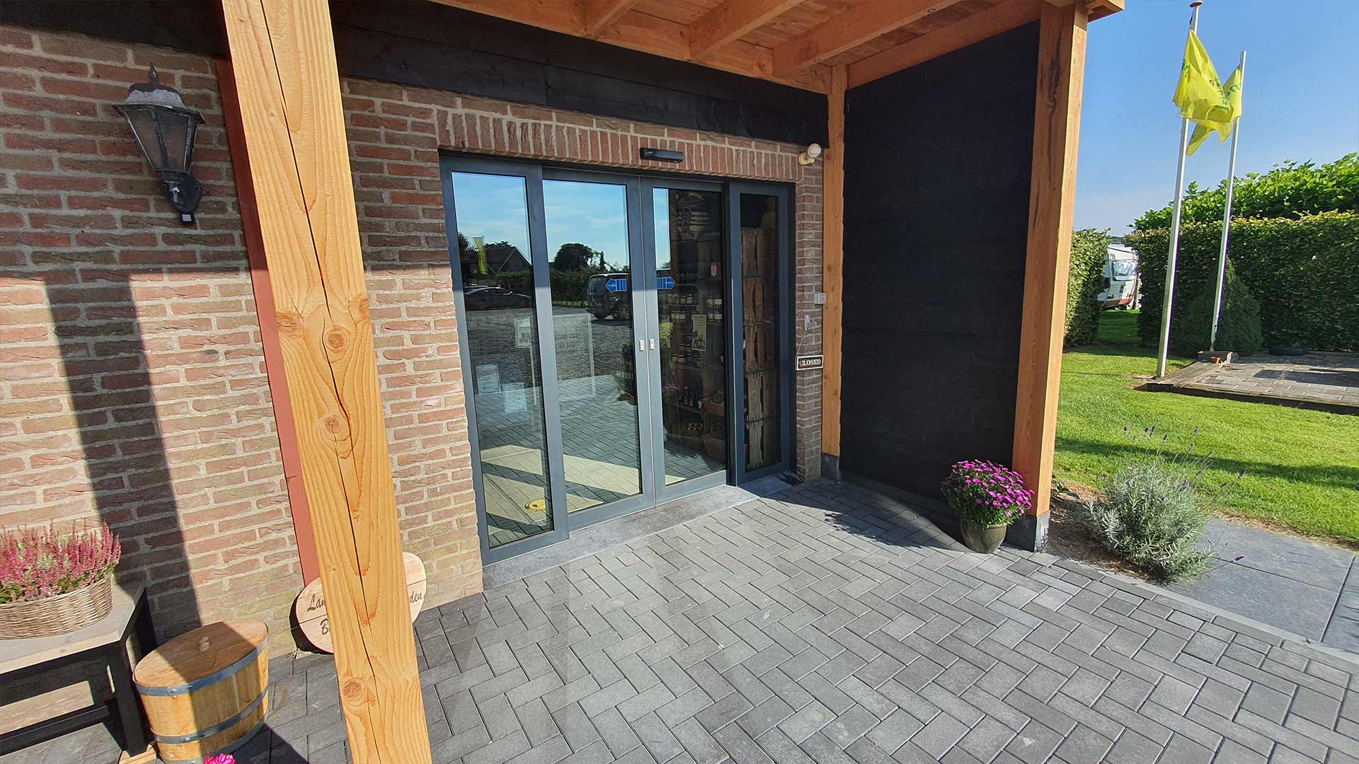 Entree met glazen deuren, stenen muren, houten balken en planten in potten.