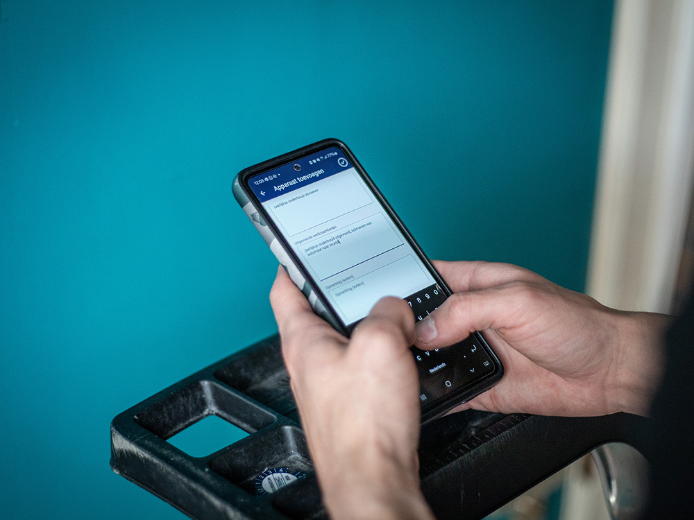 Hand die een smartphone vasthoudt, met een turquoise muur op de achtergrond.