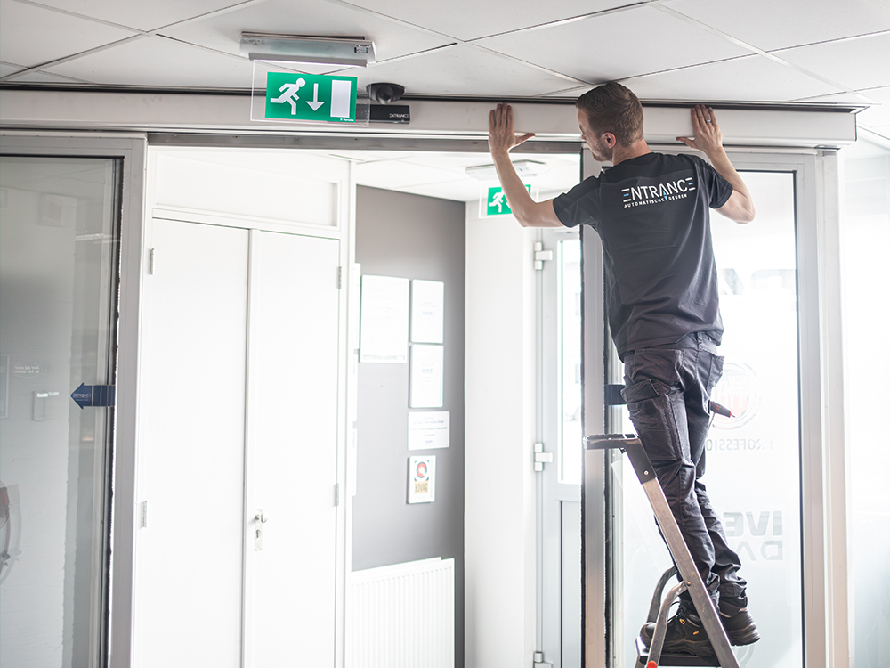 Werknemer staat op een ladder en installeert iets aan het plafond in een kantoor.