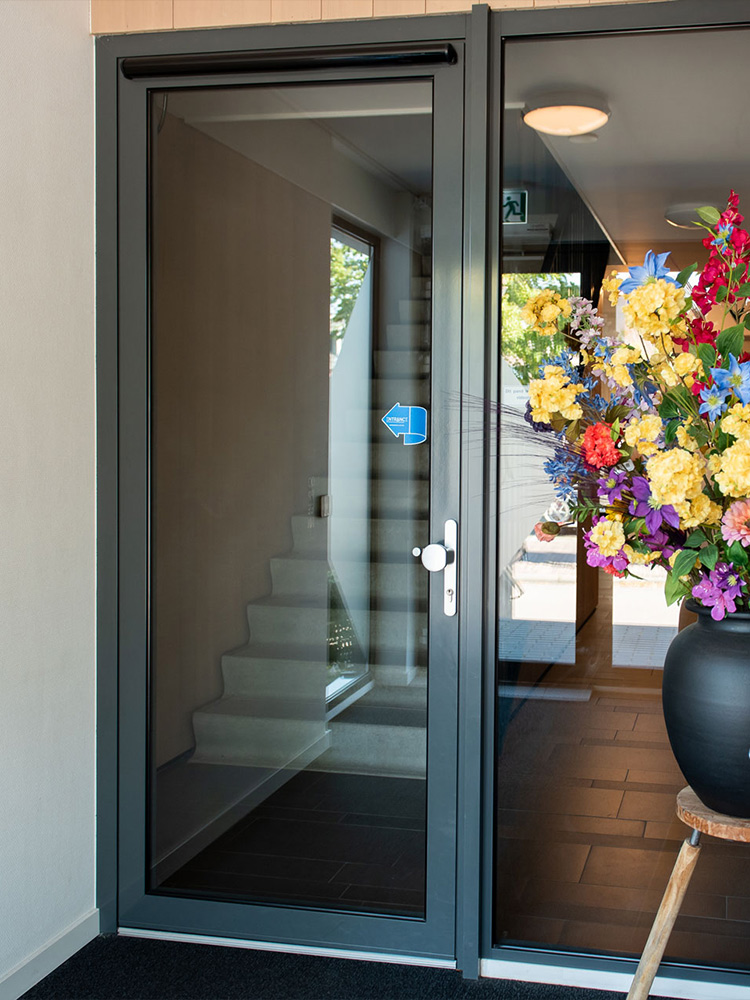 Een glazen deur met een grote vaas vol kleurrijke bloemen ernaast.