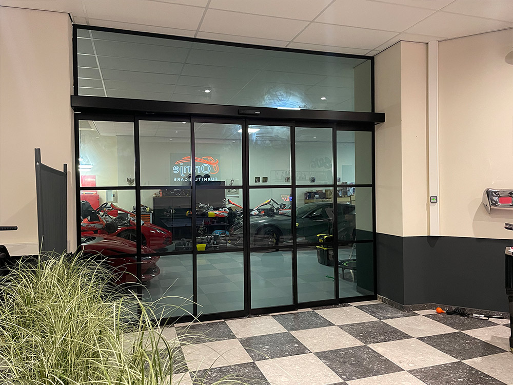 Glazen schuifdeur met uitzicht op go-karts en een auto binnen.